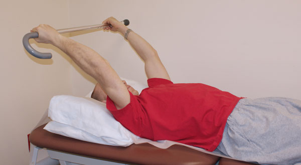 Man lying prone with arms raised holding a cane.
