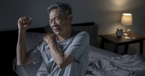 An older man holding his shoulder in pain.