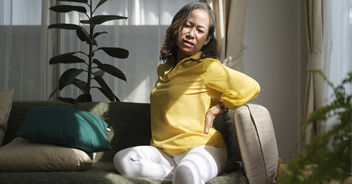 An older, middle-aged woman grabbing her low back due to pain.