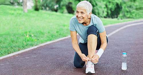 An older woman jogger bending to tie her running shoe.