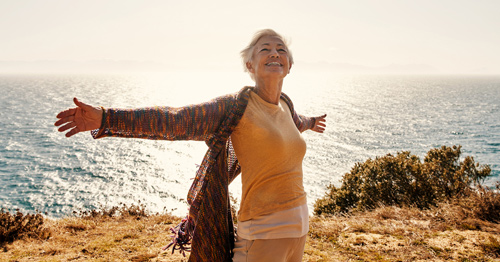 A woman smiling and stretching out her arms by the beach.