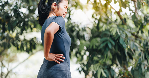 A woman grabbing her lower back and hip in pain.