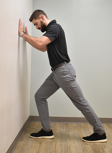 man standing with hands on a wall stretching his calf muscles